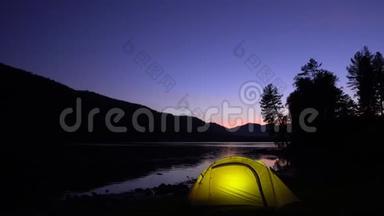 黄色帐篷在山湖畔花费.. 晚安。 在帐篷里，光线燃烧。
